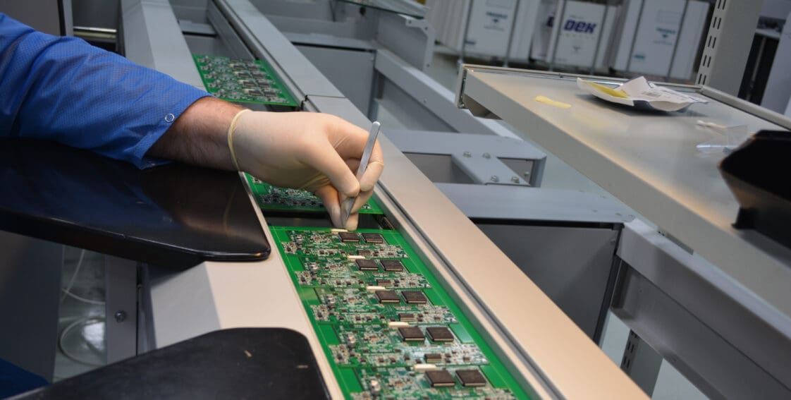 A person wearing a glove is carefully placing components on a single-sided printed board circuit.
